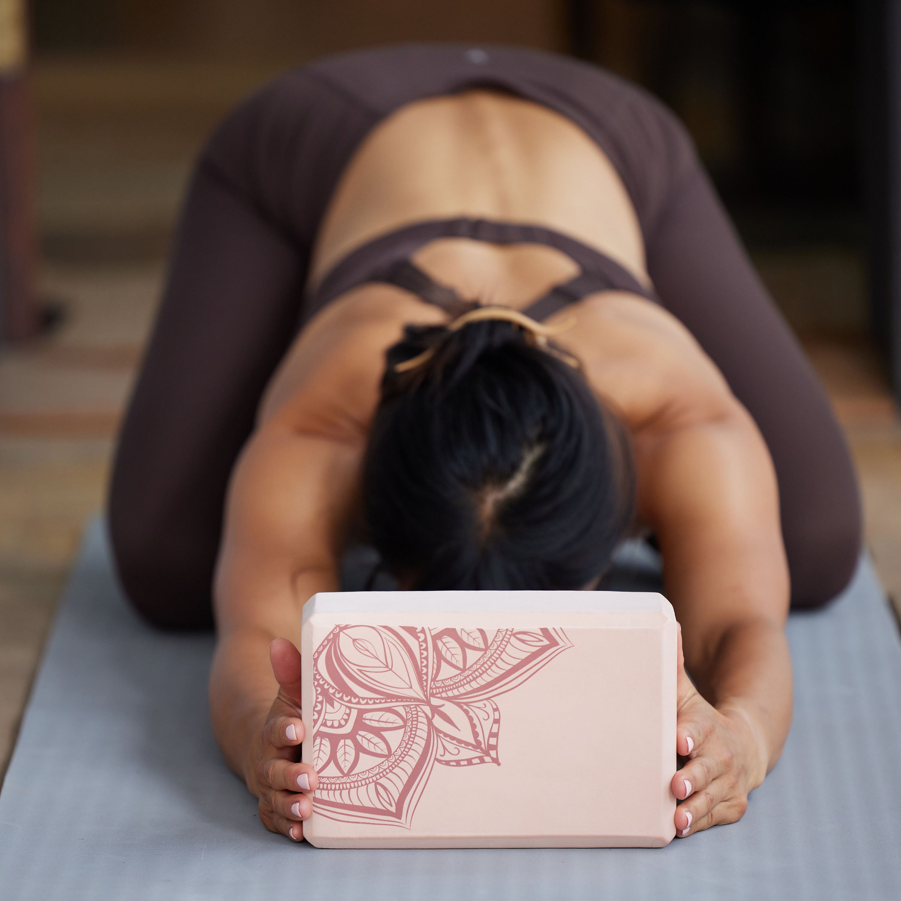 Person on mat in Childs Pose holding block between hands